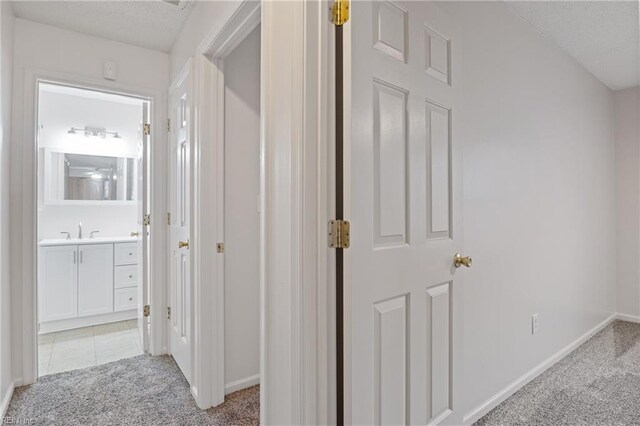 hall featuring a textured ceiling, light tile patterned flooring, light colored carpet, a sink, and baseboards