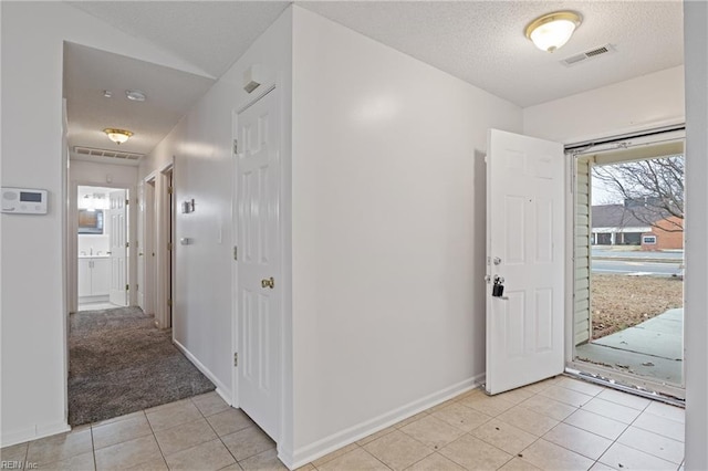 foyer with a textured ceiling, light tile patterned flooring, light carpet, visible vents, and baseboards