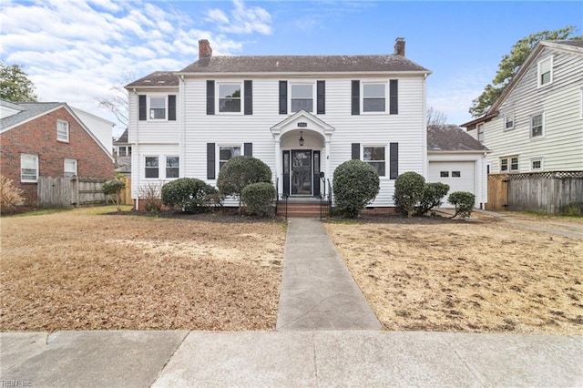 colonial inspired home with a garage, a chimney, and fence