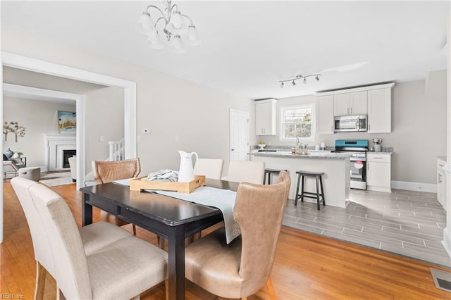 dining area with a chandelier, a fireplace, visible vents, baseboards, and light wood-style floors