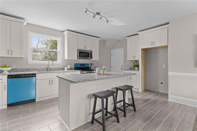 kitchen with light stone countertops, white cabinetry, a kitchen island, and appliances with stainless steel finishes