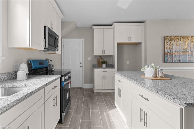 kitchen with baseboards, white cabinets, appliances with stainless steel finishes, light stone counters, and a center island