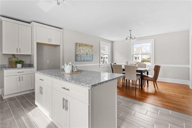 kitchen with wood finish floors, a notable chandelier, white cabinets, a kitchen island, and light stone countertops