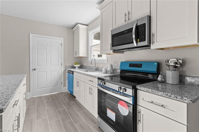 kitchen with appliances with stainless steel finishes, white cabinets, a sink, and light stone counters