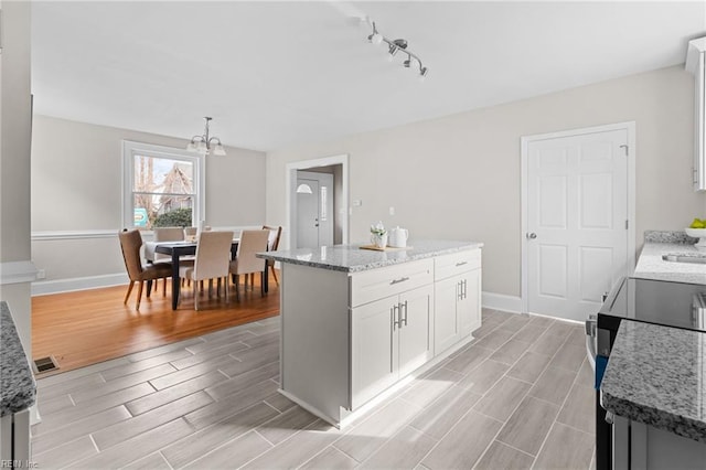 kitchen with visible vents, light stone counters, a center island, wood tiled floor, and white cabinetry