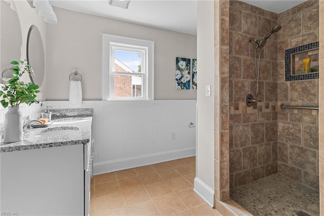 full bath with tile patterned floors, wainscoting, vanity, and tiled shower