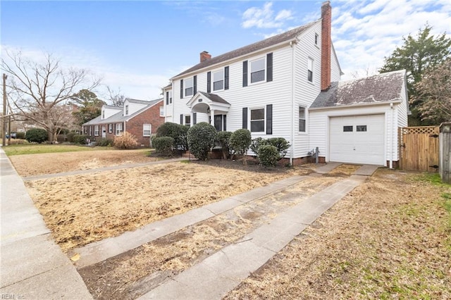 colonial-style house with driveway, a chimney, an attached garage, and fence