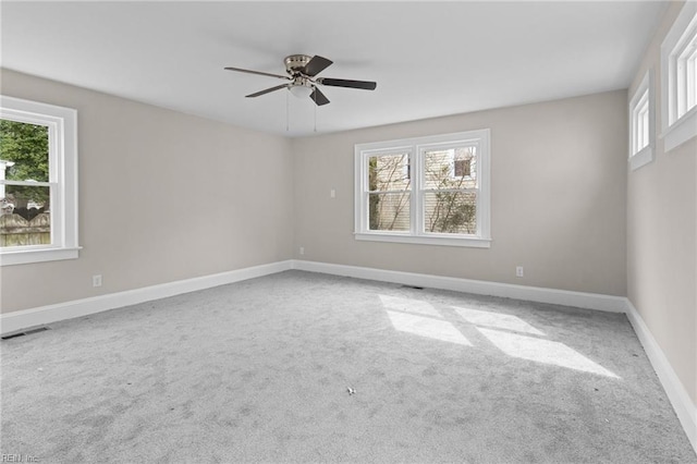 empty room with carpet floors, a ceiling fan, visible vents, and baseboards