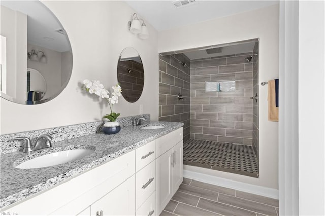 bathroom featuring double vanity, tiled shower, a sink, and visible vents