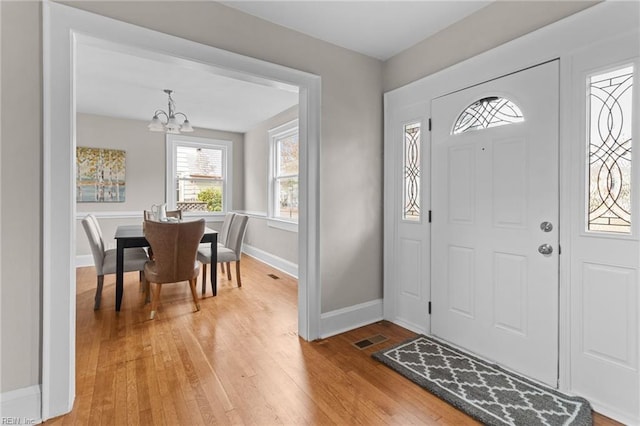 foyer with a chandelier, light wood finished floors, visible vents, and baseboards