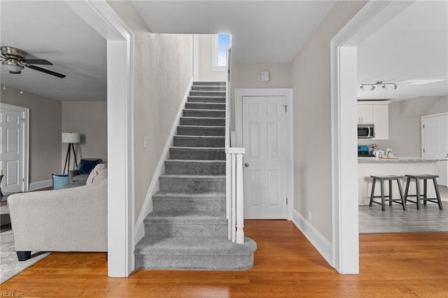 stairway featuring track lighting, ceiling fan, baseboards, and wood finished floors