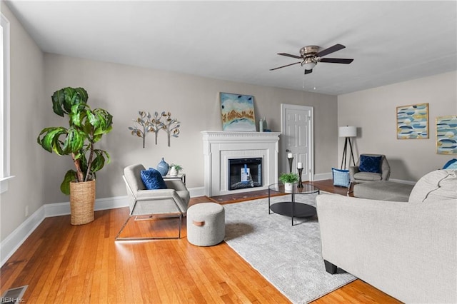 living area with a fireplace with flush hearth, wood finished floors, visible vents, and baseboards