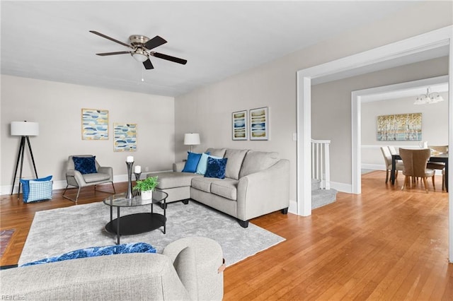 living area with light wood-style floors, baseboards, and ceiling fan with notable chandelier