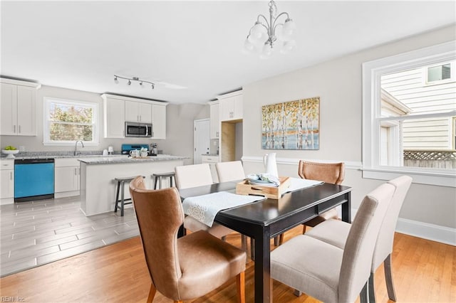 dining space featuring rail lighting, light wood-style flooring, baseboards, and an inviting chandelier