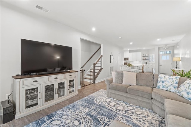 living room with light wood-type flooring, stairway, baseboards, and visible vents