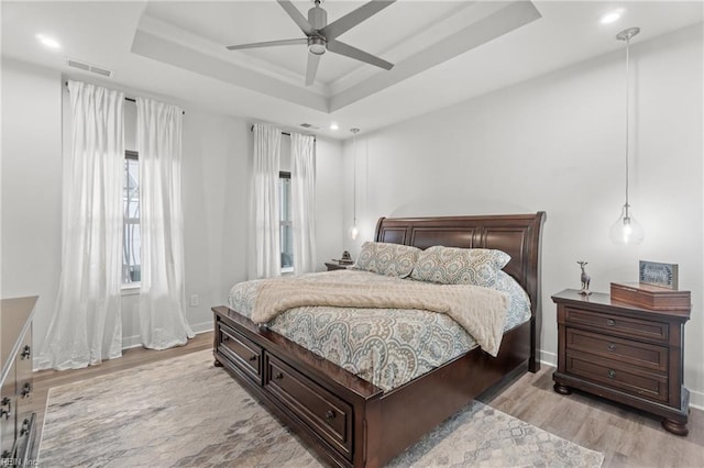 bedroom with light wood-type flooring, a raised ceiling, visible vents, and recessed lighting