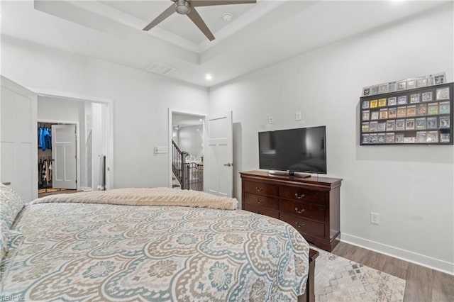 bedroom featuring wood finished floors, visible vents, baseboards, a spacious closet, and a raised ceiling