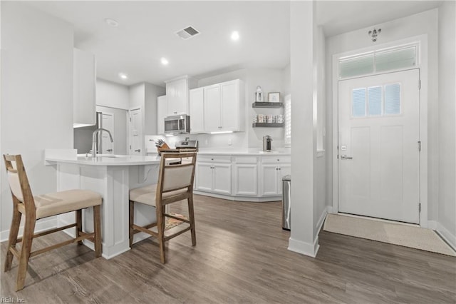 kitchen with dark wood-style flooring, a breakfast bar area, stainless steel appliances, visible vents, and white cabinets