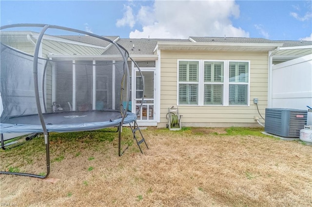 back of property featuring central air condition unit, a sunroom, a trampoline, and a yard