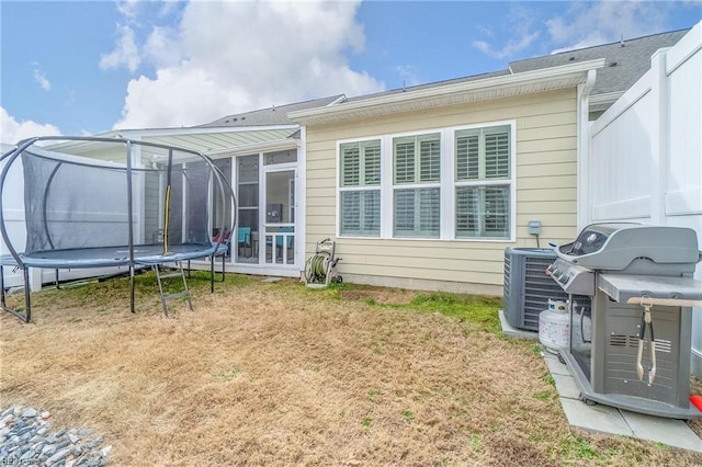 rear view of house featuring a sunroom, a trampoline, a lawn, and cooling unit