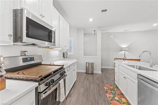 kitchen with appliances with stainless steel finishes, a sink, light wood-style floors, and white cabinets