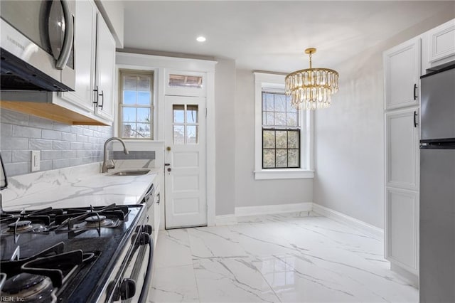 kitchen with light stone counters, marble finish floor, stainless steel appliances, a sink, and baseboards