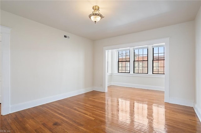 empty room with wood finished floors, visible vents, and baseboards