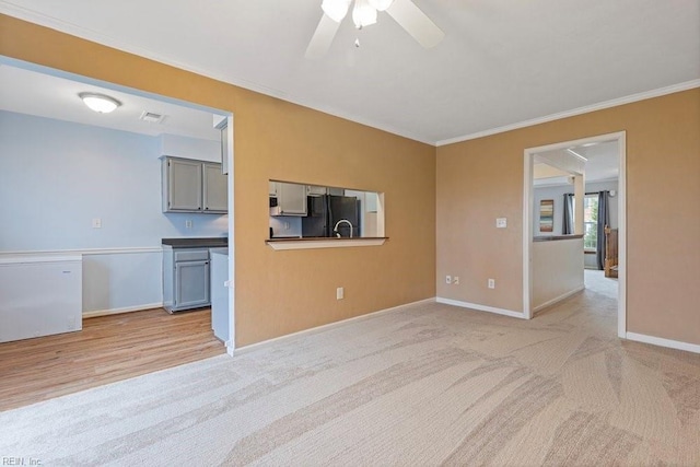 empty room featuring light colored carpet, visible vents, baseboards, a ceiling fan, and crown molding