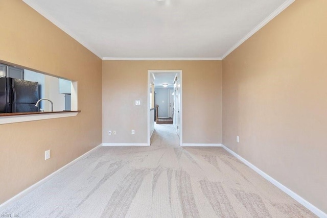 carpeted empty room featuring a sink, crown molding, and baseboards