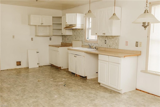 kitchen with light floors, hanging light fixtures, decorative backsplash, white cabinetry, and a sink