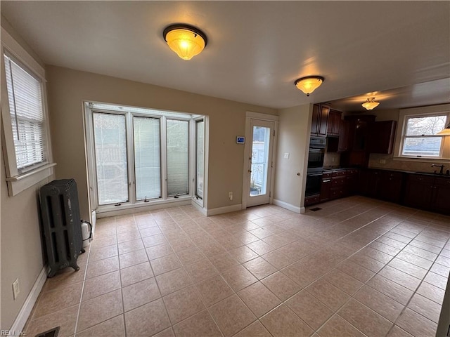 unfurnished living room with light tile patterned floors, visible vents, baseboards, radiator, and a sink