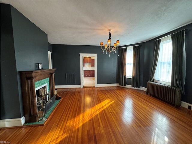 unfurnished living room featuring baseboards, a tiled fireplace, radiator heating unit, hardwood / wood-style floors, and an inviting chandelier