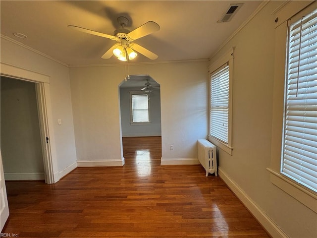 spare room with visible vents, arched walkways, radiator, ornamental molding, and wood finished floors