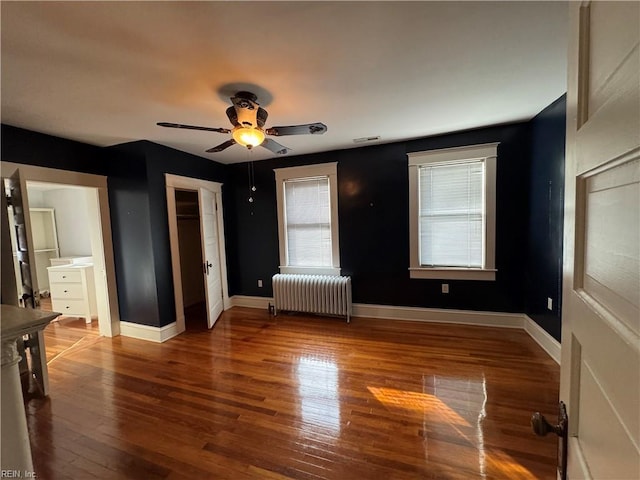 unfurnished bedroom featuring radiator, visible vents, a ceiling fan, wood finished floors, and baseboards