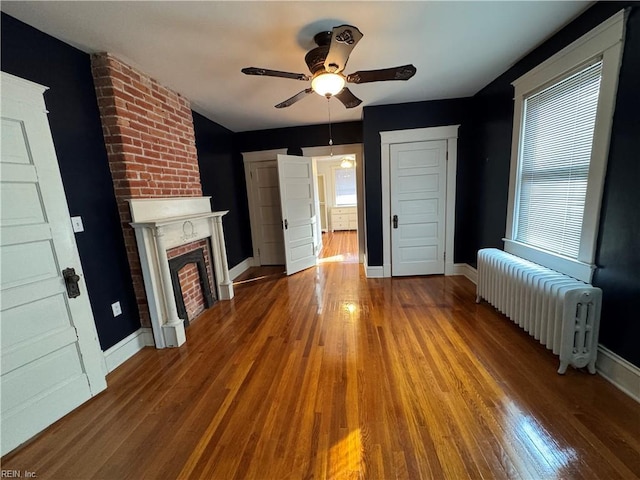 unfurnished living room with baseboards, radiator, ceiling fan, wood finished floors, and a fireplace