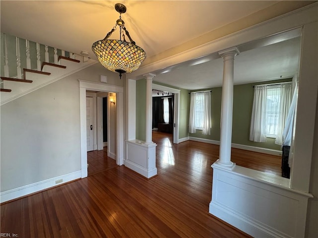 unfurnished dining area with stairs, wood finished floors, decorative columns, and baseboards