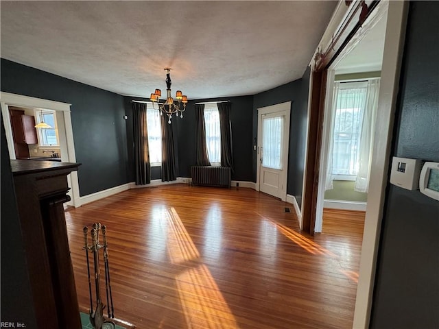 unfurnished dining area with a chandelier, baseboards, wood finished floors, and radiator