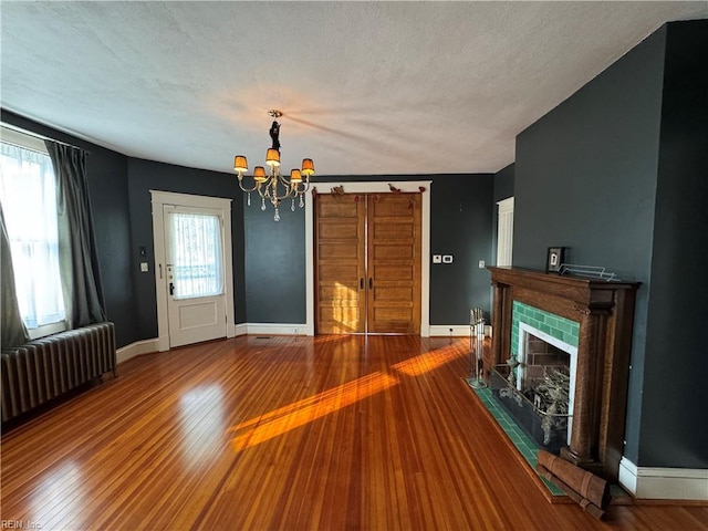 unfurnished living room with radiator heating unit, baseboards, wood finished floors, and a tile fireplace