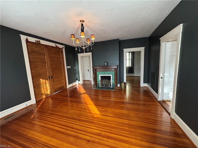 unfurnished living room with a chandelier, wood finished floors, a fireplace with flush hearth, and baseboards