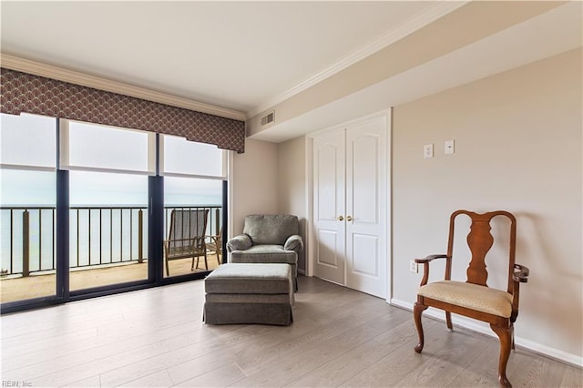 living area with ornamental molding, light wood-type flooring, visible vents, and baseboards