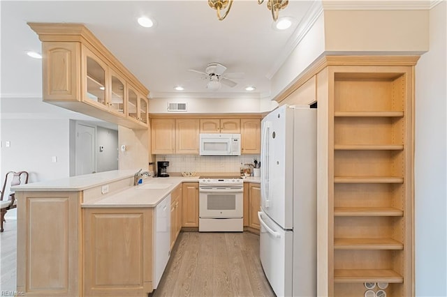 kitchen with light countertops, light brown cabinets, a sink, white appliances, and a peninsula