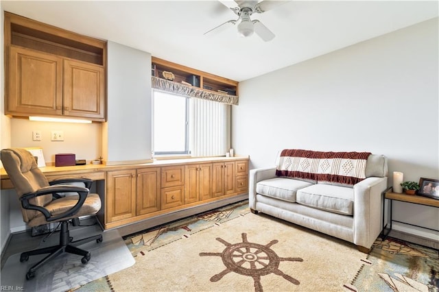 living area with a ceiling fan, built in desk, and baseboards