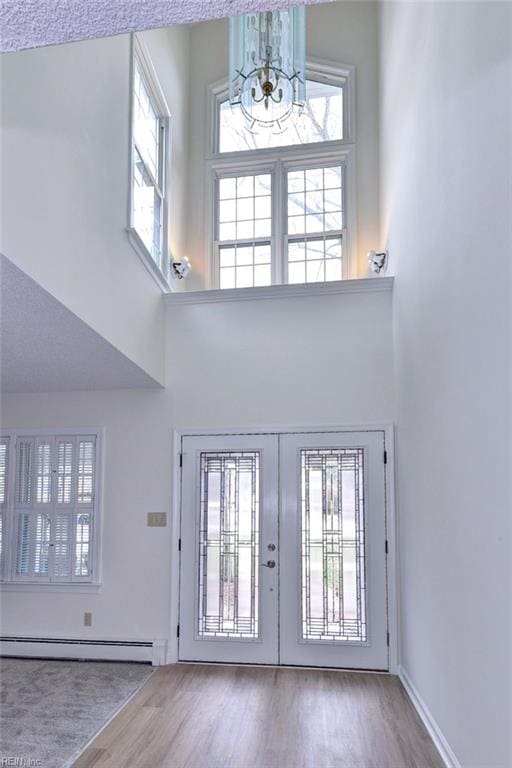 entryway with french doors, a notable chandelier, a towering ceiling, baseboard heating, and wood finished floors