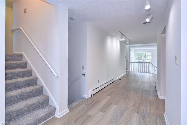 hallway featuring a baseboard radiator, light wood-style floors, a baseboard heating unit, a textured ceiling, and baseboards