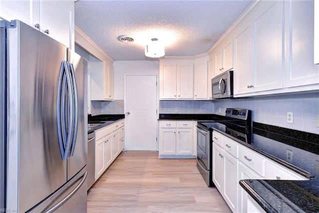 kitchen with dark stone counters, stainless steel appliances, light wood-style flooring, and white cabinetry