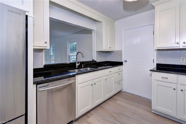 kitchen with light wood-style flooring, appliances with stainless steel finishes, dark stone countertops, white cabinetry, and a sink