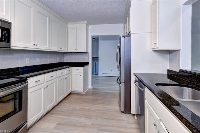 kitchen featuring stainless steel appliances, backsplash, light wood-style flooring, a baseboard heating unit, and white cabinetry