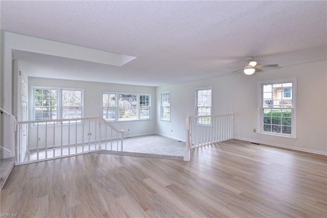 unfurnished living room with ceiling fan, a textured ceiling, baseboards, and wood finished floors