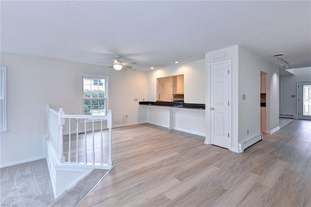 kitchen with a textured ceiling, a baseboard radiator, baseboards, and light wood-style floors