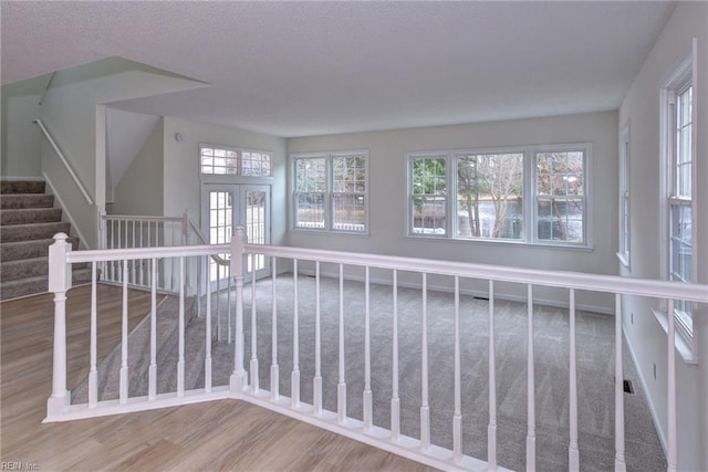 empty room with wood finished floors, french doors, a textured ceiling, and stairs